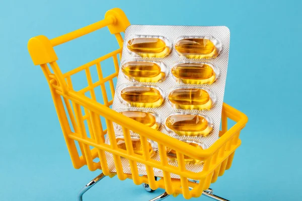 Basket loaded with vitamin D or fish oil capsules in a plate on a blue background. The concept of medicine and sales. Copy the space. Stock Photo