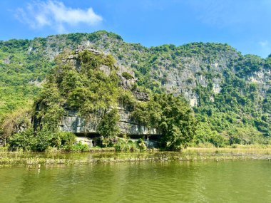 Sessiz bir göl kenarındaki kireçtaşı kayalıkları. Doğal mağaraları ve yemyeşil bitkileri olan dağ, Tam Coc - Bich Dong in the Trang An Manzara Kompleksi - Ninh Hai, Hoa Lu, Ninh Binh,