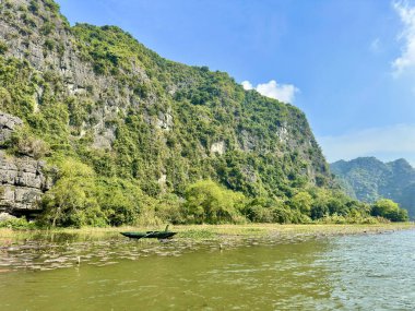 Su zambaklarıyla dolu nehir kıyısında dinlenen küçük bir tekne. Dev kireçtaşı dağının eteğindeki mutlak sessizlik, Tam Coc 'ta, Trang An Manzarası' ndaki Bich Dong 'da, miras alanının kalbinde şiirsel bir duraklamaya neden olur.