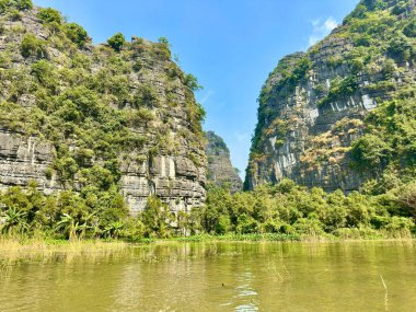Tam Coc 'taki derin mavi nehrin çevresindeki yüksek kireçtaşı dağlarının panoramik görüntüsü - Bich Dong in the Trang An Manzarası Kompleksi - Ninh Hai, Hoa Lu, Ninh Binh, Vietnam, 17 Aralık 2025. Fotoğraflarda M harfi var.