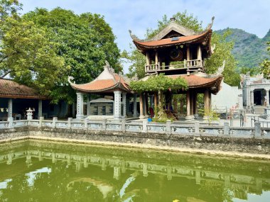 Geleneksel ahşap çan kulesi mimarisi çift katmanlı kıvrımlı çatıları temiz bir gölete yansıyor. Tayland Vi Tapınağı, Tam Coc - Bich Dong, Ninh Binh, Vietnam, 17 Aralık 2025. Zarif kıvrımlı kiremit çatılı ahşap yapı