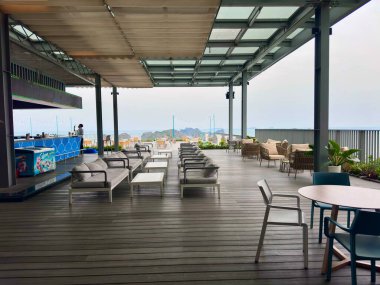 Lan Ha Sky Bar 'ın panoramik manzarası ve Lan Ha Körfezi üzerinde sonsuz manzarası var. Görüntü, modern gri kanepeler ve denize bakan büyüleyici kahve masalarıyla sıralanmış koyu kahverengi ahşap döşeme ile geniş bir açık alanı kaplıyor. Flam 'de Yakalandı