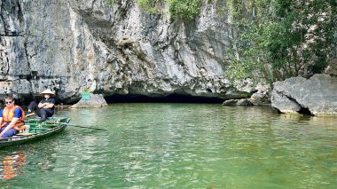 Tam Coc bölgesinde kristal berrak yeşil suyla kireçtaşı mağara girişinin saf güzelliği. Kireç taşı mağarasının girişinde sarkıtlar derin yeşil suya doğru sarkan yakın çekim. Tam Coc - Bich Dong, Ninh Binh, Vietnam, Decembe