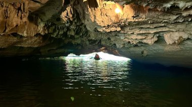 Tam Coc Bich Dong mağarasında yolcuları taşıyan küçük bir tekne yavaşça ışığa doğru sürükleniyor. Yolcuları taşıyan bir tekne kireçtaşı mağarasının çıkışına doğru ışığa doğru ilerliyor. Tam Coc - Bich Dong, Ninh Binh, Vietnam, 10 Aralık 2025. Çeviri: