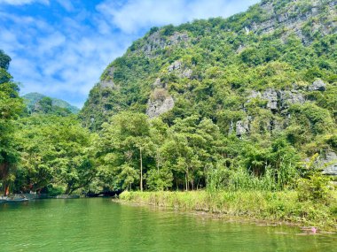 Yeşil çimen halısı ve Tam Coc Ninh Binh manzaralı dağları olan taze doğal manzara. Fotoğraf otlaklar, yeşil nehir ve görkemli kireçtaşı çıkıntıları arasındaki ahenkli geçişi yakalar..
