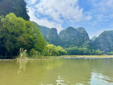 Vietnam 'daki muhteşem kireçtaşı kayalıkları boyunca canlı yeşil ağaçlarla büyüleyici nehir manzarası. Fotoğraf, yeşil yaprak ve gri kayanın uyumlu kombinasyonuyla rahatlama hissi veriyor. Tam Coc - Bich Dong, Ninh Binh, Vietnam