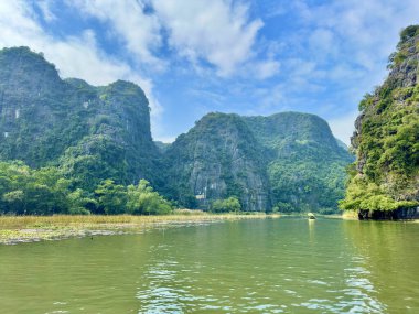 Şairane Ngo Dong Nehri 'nin panoramik manzarası muhteşem ve yuvarlanan kireçtaşı sıradağları boyunca kıvrılıyor. Fotoğraf, toprak, su ve gökyüzünün kesiştiği yer olan miras bölgesinin muazzam güzelliğini yansıtıyor. Tam Coc - Bich Dong, Ninh Binh