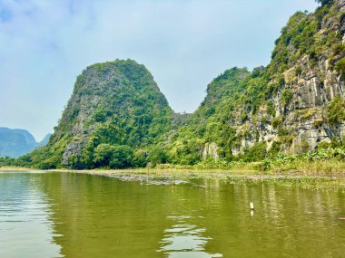 Tam Coc 'un manzaralı bölgesinde dağlarla sessiz bir göl arasındaki kavşak. Kireçtaşı dağları derin mavi nehre yansıyarak havadar ve saf bir uzay yaratır. Tam Coc - Bich Dong, Ninh Binh, Vietnam 10 Aralık 2025