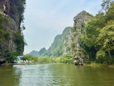 Ninh Binh ilindeki Tam Coc turizm sahasındaki nehir manzarası ve görkemli kireçtaşı dağları. Fotoğraf, Zümrüt Su 'yu yansıtan dikey kireçtaşı kayalıklarının olduğu Ngo Dong Nehri' nden geniş bir görüntü yakalıyor.