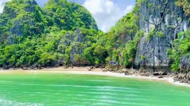 Yüksek sürat teknesi körfezdeki el değmemiş beyaz kumlu plajların ve kireçtaşı kayalıkların yanından geçiyor. Dağların eteklerinde kristal berrak suyla gizlenmiş küçük kumsallar. Bai Tu Long Bay, Quang Ninh, Vietnam 16 Temmuz 2025. Saf, el değmemiş bir güzellik