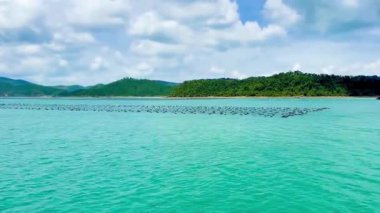 Derin mavi deniz yüzeyi boyunca uzanan yüzen şamandıraları olan su kültürü alanı. Küçük bir balıkçının teknesi istiridye çiftliği şamandıralarının arasından süzülüyor. Bai Tu Long Bay, Quang Ninh, Vietnam 16 Temmuz 2025. Yerel ve balıkçı köylerinin tipik bir manzarası.
