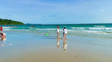 Van Chay Sahili kıyısında mavi suyla güzel fotoğraflar çeken iki genç kız. Video, pürüzsüz beyaz kumda fotoğraf çektirmek için poz veren sığ sularda parıldayan bir grup kadın arkadaşı yakalıyor.