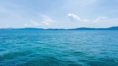 Zümrüt deniz yüzeyi, Quang Ninh vilayetindeki uzak sisli dağlarla ufka kadar uzanıyor. Video, yaz güneşi altında hafif dalgalanmalarla okyanusun sakin güzelliğini yakalıyor. Bai Tu Long Körfezi, Quang Ninh, Vietnam