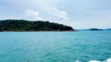 Sonsuz yemyeşil orman dağları Bai Tu Long Bay Vietnam 'ın zümrüt kıyı şeridi boyunca uzanıyor. Hızla süzülen tekne, yuvarlanan dağ manzarasının yanında beyaz uyanışlar yaratır. Bai Tu Long Körfezi, Quang Ninh, Vietnam 22 Temmuz 2025.