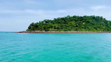 Bai Tu Long Körfezi deniz bölgesindeki el değmemiş bir adanın kayalık sahili çok yakında. Tekne çakıl taşları ve koyu yeşil ormanlı bir pelerini geçerek uzak adalara doğru geniş bir görüş açısı sağlıyor. Bai Tu Long Körfezi, Quang Ninh, Vietnam 22 Temmuz 2025