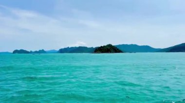 Uçsuz bucaksız mavi Bai Tu Long Körfezi 'nin ortasında tek başına duran yemyeşil bir ada. Video, zümrüt yeşili suların ortasındaki sık ağaçların olduğu tek bir adaya odaklanıyor. Bai Tu Long Körfezi, Quang Ninh, Vietnam, 22 Temmuz 2025 'de yakalandı.