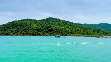 Bai Tu Long Bay adasının yemyeşil kıyısında küçük bir balıkçı teknesi. Video, kireçtaşı bir dağın eteğinde, derin mavi bir su arka planına karşı faaliyet gösteren küçük bir teknenin yakın çekimini kaydediyor. Bai Tu Long Körfezi 'nde yakalandı.