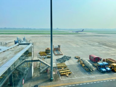Uluslararası havaalanı apron alanındaki pist alanı ve yer destek ekipmanlarının genel görünümü. Yukarıdan bakıldığında, bagaj traktörleri, rampalar ve teknik ekipmanlar önlüğün üzerine park edilmiştir. Noi Bai Havaalanı, Hanoi, Vietnam