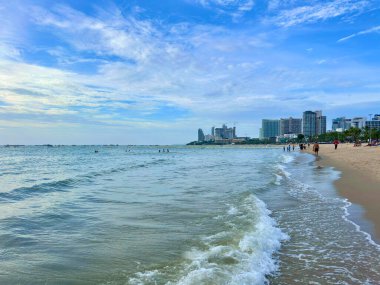 Turistler Tayland 'da Pattaya sahilinde yüzerken kumlu kıyıya küçük dalgalar çarpıyor. Sudan yüksek binalara bakan alçak açılı çekim ve tatilin tadını çıkaran turistler. Pattaya Sahili, Tayland 29 Temmuz 2025.