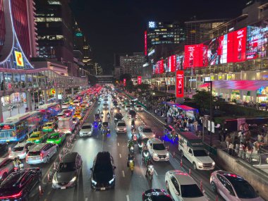 Bangkok 'taki Big C Rajdamri bölgesinde parlak kırmızı reklam ışıkları altında hareketli bir trafik akışı. Sokak, motosiklet farlarının, arabaların renkleri ve büyük reklam panolarından yansıyan kırmızı ışıklarla dolu. Bangkok 'ta yakalandı.