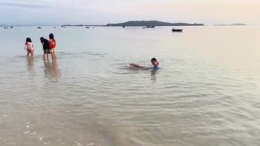 Çocuklar sabah Hong Van plajı boyunca yürüyüp yengeç ve salyangoz avlıyor. 20 Temmuz 2025 'te, Hong Van Sahili, Co To Island, Quang Ninh, Vietnam' da sığ sularda kıyı ekosistemini keşfeden bir grup çocuk