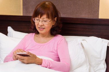 Kıdemli yatakta telefon ile rahatlatıcı