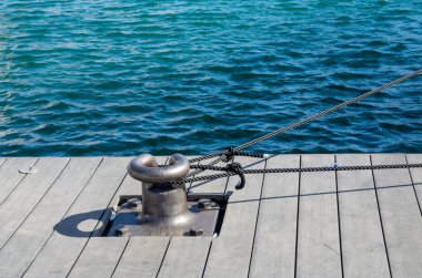 A large mooring post for a sea vessel on a wooden pier with anchor ropes attached
