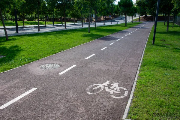 Parkta bisiklet yolu üzerinde beyaz bir bisiklet sembolü asfalta boyanmış ve şeritleri ayıran kesik bir çizgi var. Yeşil kentsel bir çevrede açık hava bisiklet yolu, eğlence, uygunluk ve sürdürülebilir ulaşım için ideal. Cy için güvenli ve iyi işaretlenmiş rota