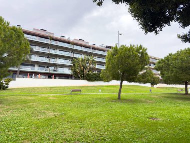 Sitges, İspanya Ocak 2026 Konut kompleksi birden fazla katlı ve ağaçlı yeşil çimlerin arkasında geniş teraslı. Modern şehir konutları ve Akdeniz mimarisi.
