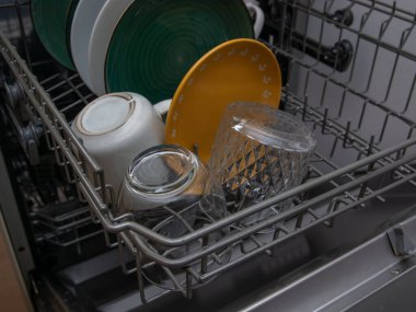 Yıkandıktan sonra bardaklar ve tabaklarla dolu açık bir bulaşık makinesi. Modern mutfak aletleri ve temiz sofra takımı konsepti, ev rutini, temizlik ve ev temizliğini gösteriyor.