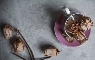 Hafif arka planda solmuş güller. Pembe bardakta kurumuş güller.