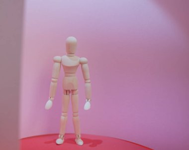 Ahşap adam kırmızı ve pembe arka planda duruyor.