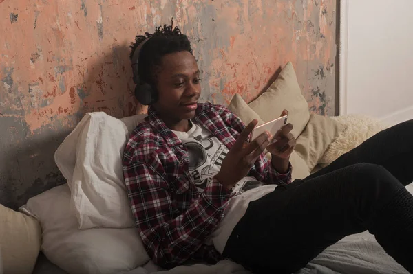Ung Afrikansk Amerikan Ligger Sängen Med Hörlurar Och Tittar Telefonen — Stockfoto