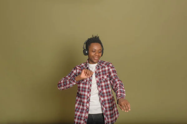Young african american guy listens to music on headphones and dances on a green background