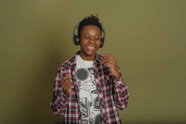 Young african american guy listens to music on headphones and dances on a green background — Stock Photo, Image
