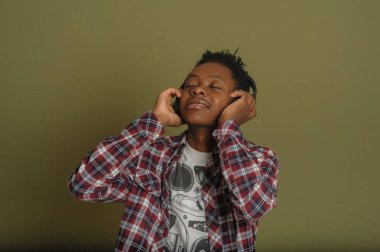 Genç Afrikalı Amerikalı adam kulaklıkla müzik dinliyor ve yeşil arka planda dans ediyor.