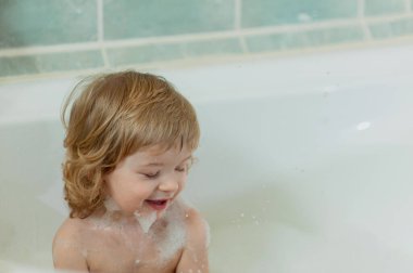 Köpük banyosunda sarı kıvırcık saçlı çocuğun yakın plan portresi.
