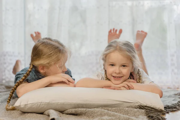 Twee kleine meisjes zusjes liggen op hun buik op de vloer thuis en glimlachen Rechtenvrije Stockafbeeldingen