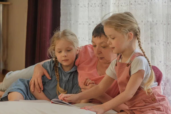 Grand-mère lit un livre à deux petites-filles à la maison Image En Vente