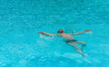 Yazın güneşli bir günde bir adam havuzda sırt üstü yüzer.