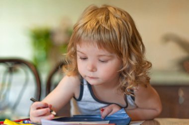 Küçük kıvırcık çocuk renkli kalemle resim çiziyor.