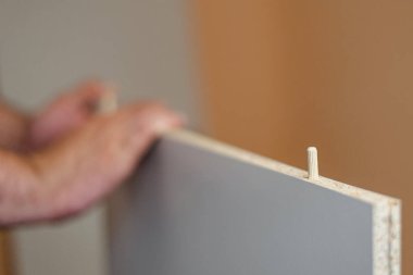 Bir adam beyaz bir tahtanın içindeki deliğe bir mobilya yerleştiriyor.