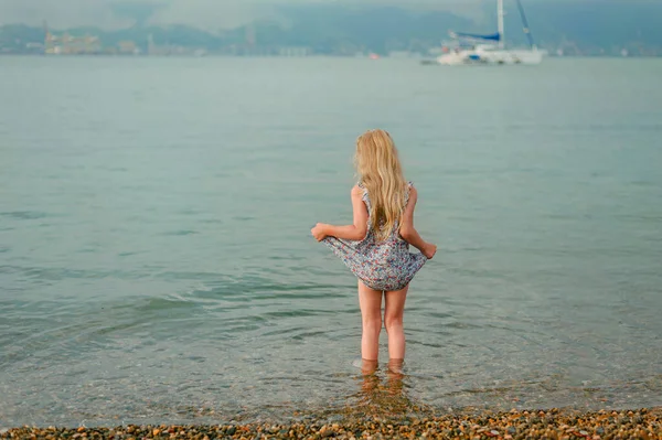Little girl stands in the sea and holds a dress so as not to soak — Stock Photo, Image
