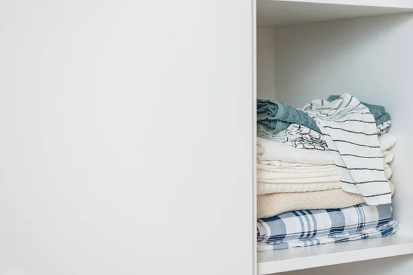 Аккуратная стопка домашнего текстиля в светлых тонах лежит на полке в белом шкафу — стоковое фото