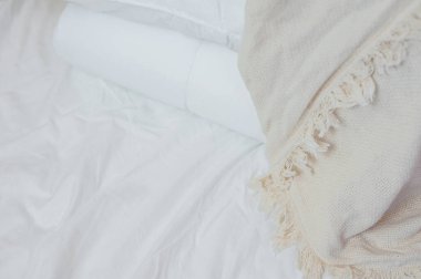 Beyaz yastık ve battaniye yığını beyaz bir çarşafın üzerinde yatar, battaniyeyle örtülü.