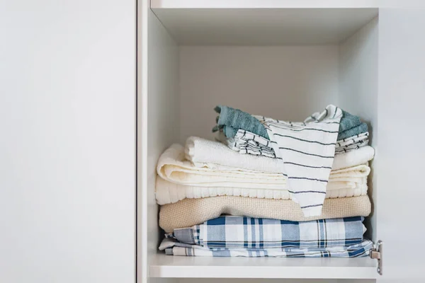 Аккуратная стопка домашнего текстиля в светлых тонах лежит на полке в белом шкафу — стоковое фото