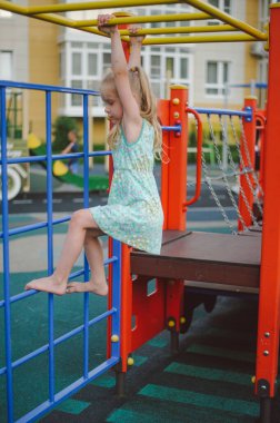Kız yazın oyun parkında yatay bir barda asılı duruyor.