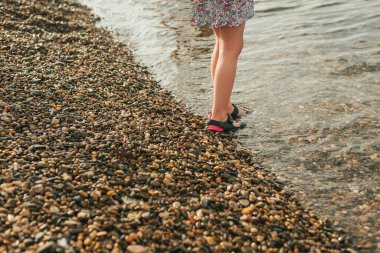 Plastik sandaletlerle çıplak ayaklı çocuklar yaz mevsiminde deniz kıyısında bir çakıl taşı plajında dururlar.