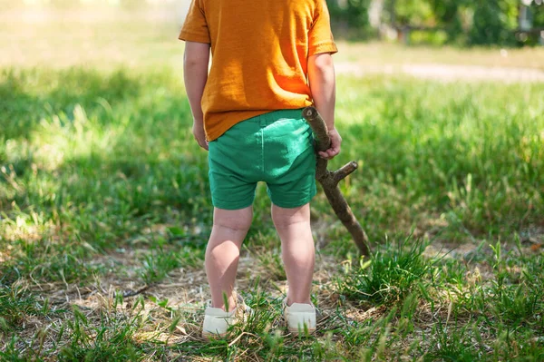 Kind staat met zijn rug met een grote stok in zijn handen in de zomer — Stockfoto