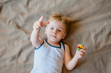 Küçük bir çocuk yatağa uzanıyor, bir lego yapıcısını elinde tutuyor ve parmağını gösteriyor.